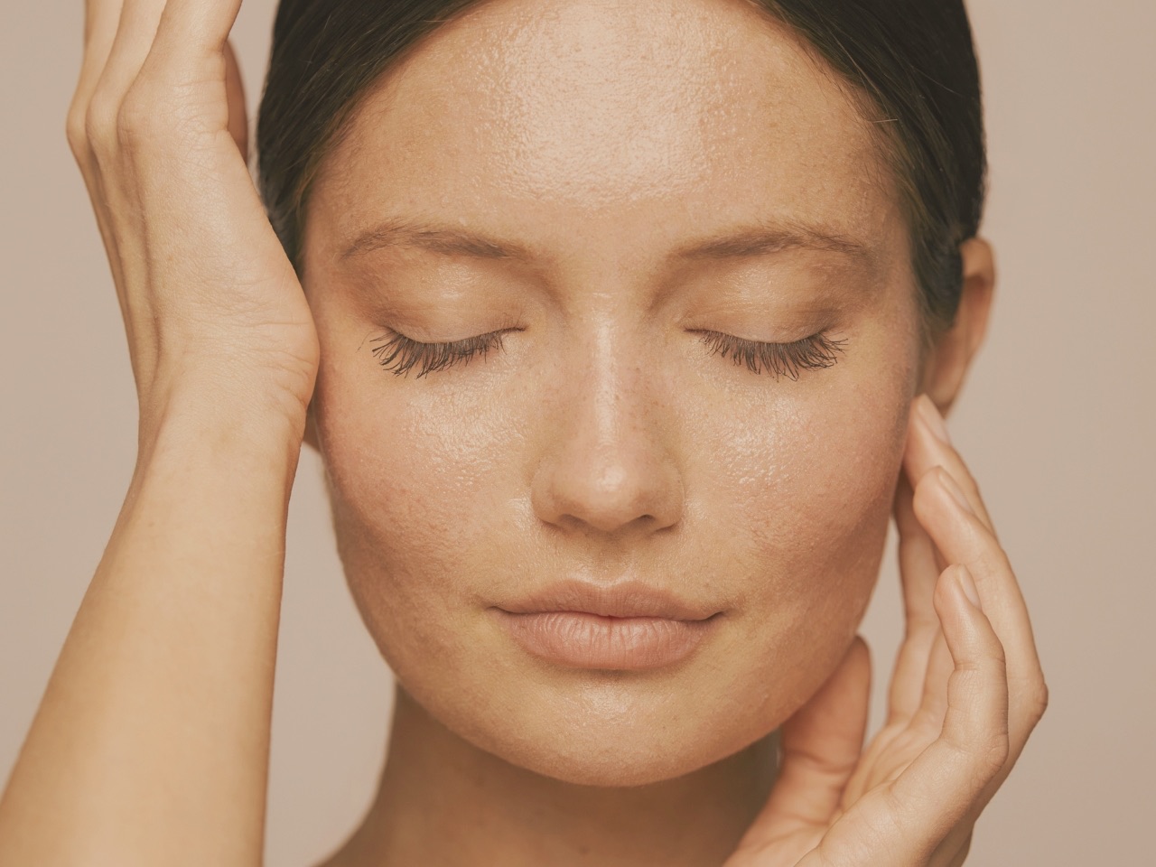Mulher de olhos fechados com pele hidratada e luminosa, iluminada por luz natural