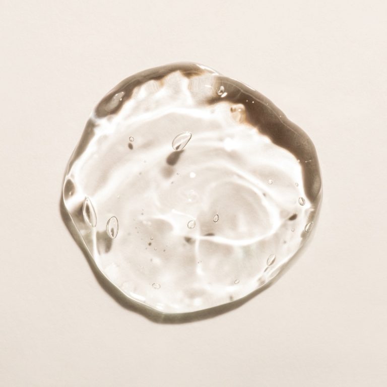 Gota de gel de ácido hialurónico sobre fundo bege, ilustrativa do tratamento com skinbooster